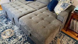 Un canapé gris à motifs en forme de touffes, agrémenté de coussins à motifs floraux, une petite table d’appoint et un tapis à motifs.