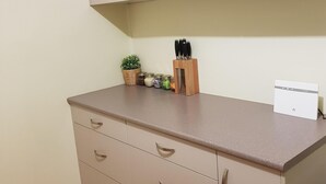 Una kitchenette con una encimera, una pequeña planta en maceta, un juego de cuchillos y un electrodoméstico blanco.