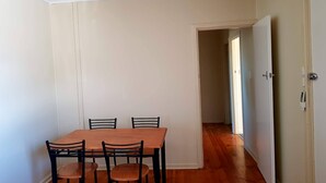 Un comedor con una mesa de madera y cuatro sillas, una puerta blanca y un pasillo que conduce a otra habitación.