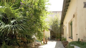 A wooden pathway leading through a garden area with potted plants and a building with a stone facade. - Montpellier center cozy house (Montpellier)