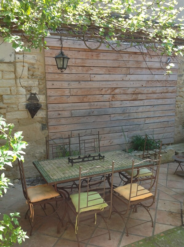 A rustic outdoor patio with a wooden table and metal chairs, a stone wall, and a hanging lantern. - Montpellier center cozy house (Montpellier)