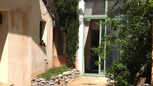 A courtyard with a stone pathway leading to a wooden door, surrounded by greenery and a stone wall. - Montpellier center cozy house (Montpellier)
