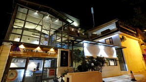 Ein modernes Hostel mit Glasfassade, Außenplätzen und einem Schild, das internationale Reiseleistungen anzeigt.