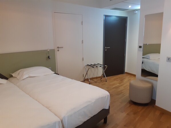 A hotel room with two beds, a wooden floor, a small stool, and a door with a towel rack. - Hôtel du Parc (Lons-le-Saunier)