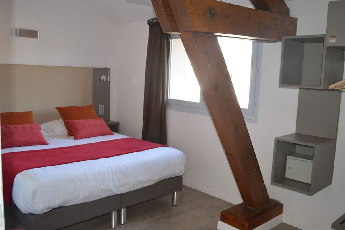 Ein modernes Schlafzimmer mit einem großen Bett, Holzbalken, einem Nachttisch und einer kleinen Ablagefläche.