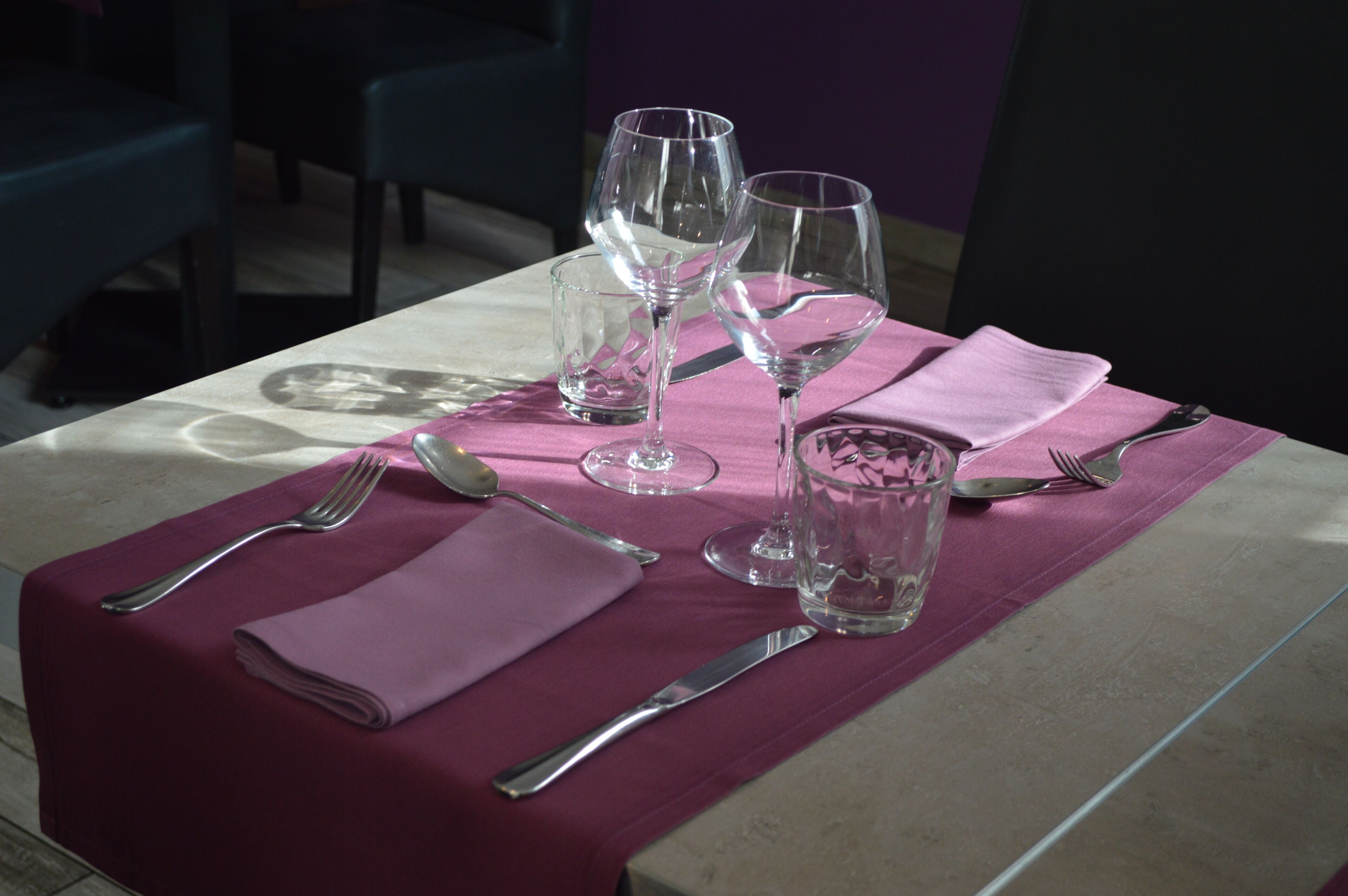 Una mesa servida con copas de vino, un vaso de agua, cubiertos y una servilleta doblada sobre un mantel.