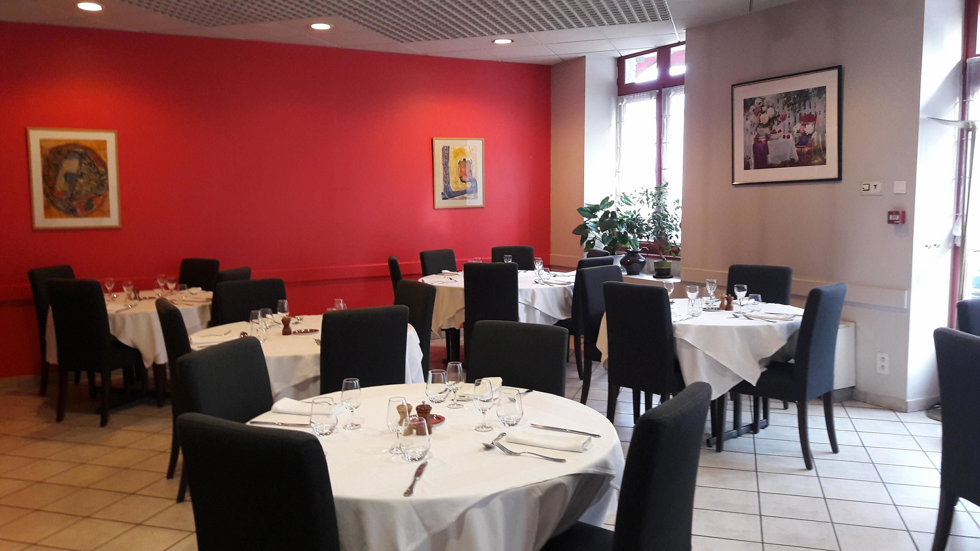 A dining area with round tables set for four, each with white tablecloths, black chairs, and basic table settings.