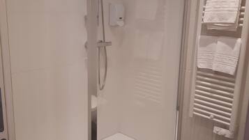 A modern bathroom with a glass shower enclosure, a white towel rack, and a towel warmer.