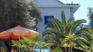 An outdoor patio with a white building, a table, chairs, and potted plants. - Holiday apartment with sea view and mountains view (Marathokampos)