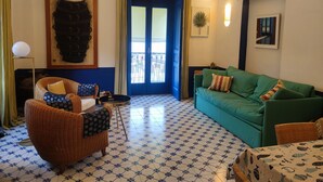 Un salón con suelo de baldosas azules y blancas, un sofá verde, un sillón de mimbre y una pequeña mesa.