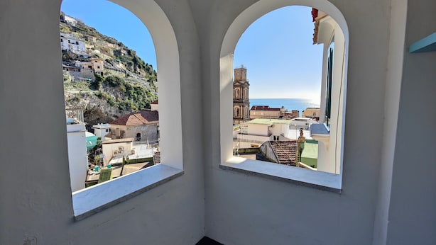 Una habitación con dos ventanas arqueadas que ofrecen vistas a un pueblo costero, incluyendo una iglesia y edificios en una colina.