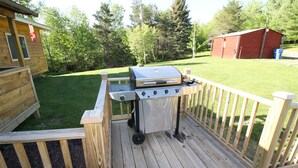 Una terraza con una parrilla, piso de madera y jardín con árboles.