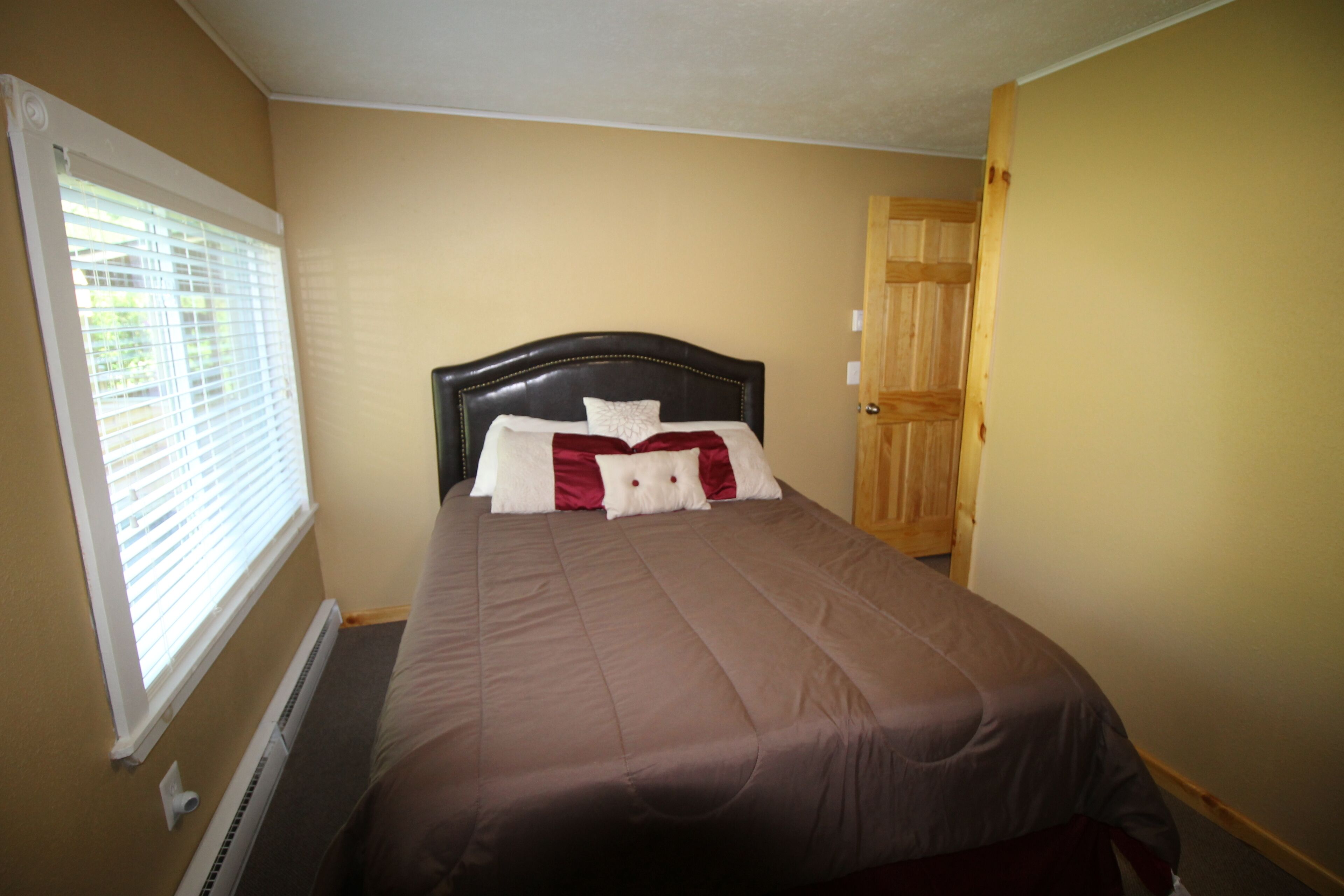 A bedroom with a bed, a window with blinds, a door, and a wall-mounted heater.