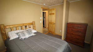 Un dormitorio con cama, cabecera de madera, cómoda y puerta que da a otra habitación.