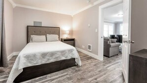A modern bedroom with a large bed, bedside tables, and a view into another room. - DOWNTOWN TACOMA HOUSE OF GRAY #4 (Tacoma)
