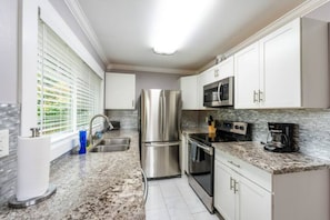 A modern kitchen with stainless steel appliances, white cabinets, and a granite countertop. - DOWNTOWN TACOMA HOUSE OF GRAY #4 (Tacoma)