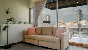 Un salon moderne avec un canapé beige, un lampadaire et une grande fenêtre donnant sur un paysage urbain.