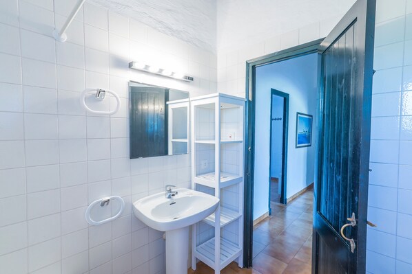 A bathroom with white tiles, a sink, a mirror, and a door leading to another room. - Beautiful Holiday Home in Residential Complex with Pool, Wi-Fi, Terrace and Lawn (Binisafua)