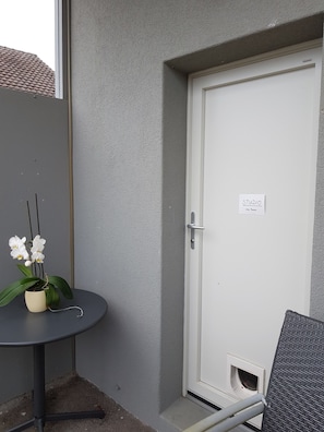 A corner of a room with a white door labeled "STUDIO," a small table with a potted orchid, and a wicker chair. - chez moumie (La Grande-Béroche)