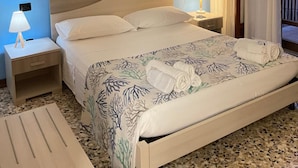 Une chambre d’hôtel avec un lit, deux tables de chevet avec des lampes, un tableau au mur et une vue sur le balcon extérieur.