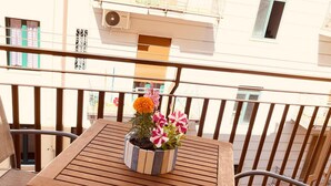 Un balcon avec une table et des chaises en bois, un pot de fleurs, et une vue sur un immeuble doté de balcons et de fenêtres.