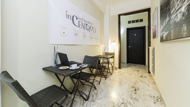 Une chambre d’hôtel avec un coin petit-déjeuner comprenant une table avec des chaises, un ordinateur portable et une tasse. Il y a une affiche au mur et une porte qui donne sur une autre pièce.