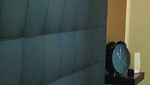 A dark-colored sofa against a beige wall with a black alarm clock on a small table beside it. - B&B In Centro 33 Home (Salerno)