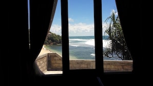 A view through a window with a beach and ocean in the background. - Omah Sundak Homestay (Wonosari)