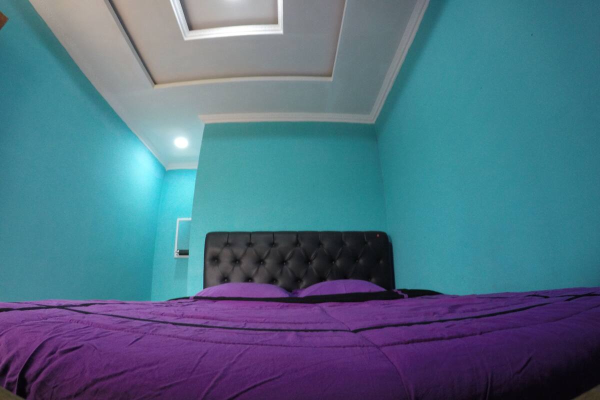 A room with teal walls, a black tufted headboard, and a purple bedspread.