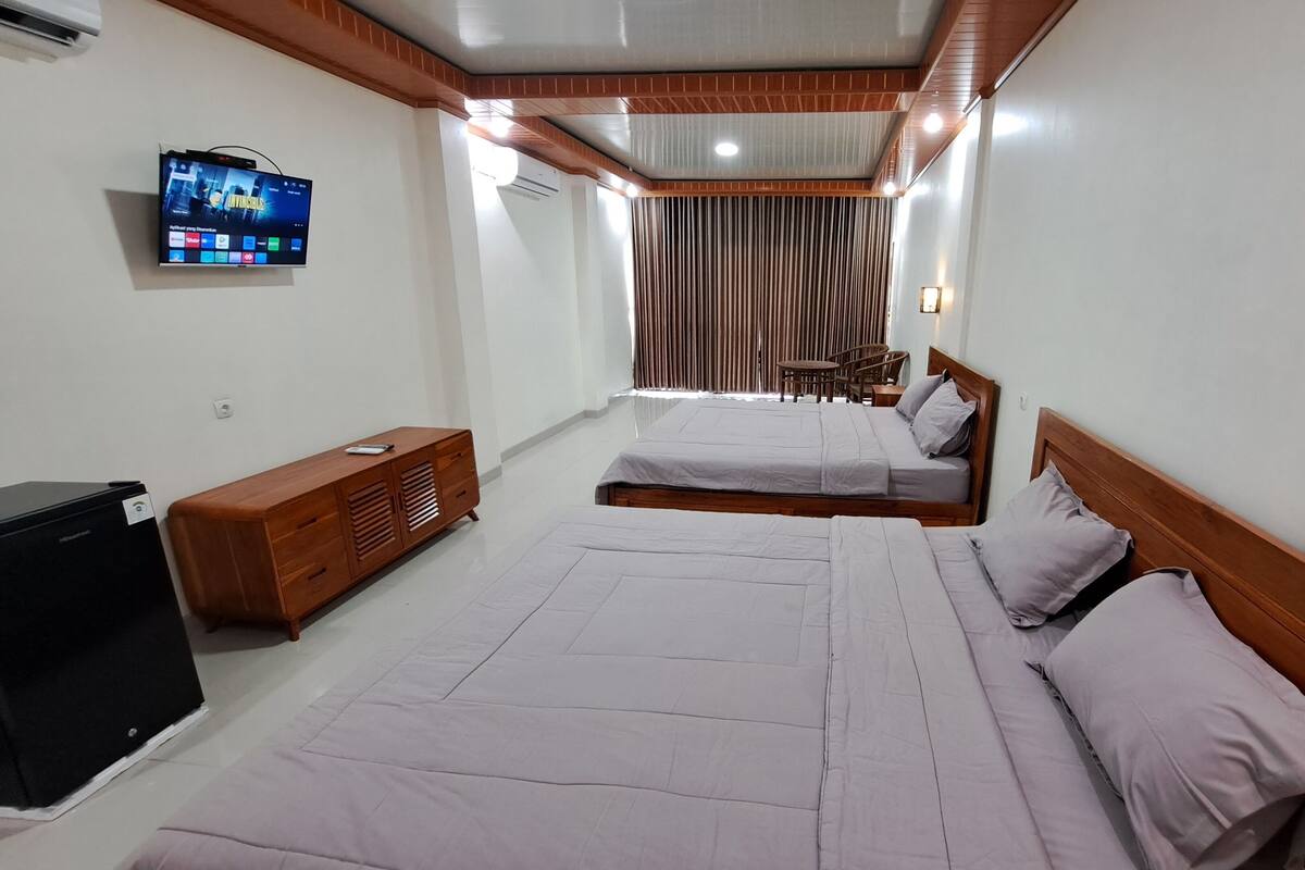 A hotel room with two beds, a TV mounted on the wall, a wooden cabinet, and a desk with a chair.