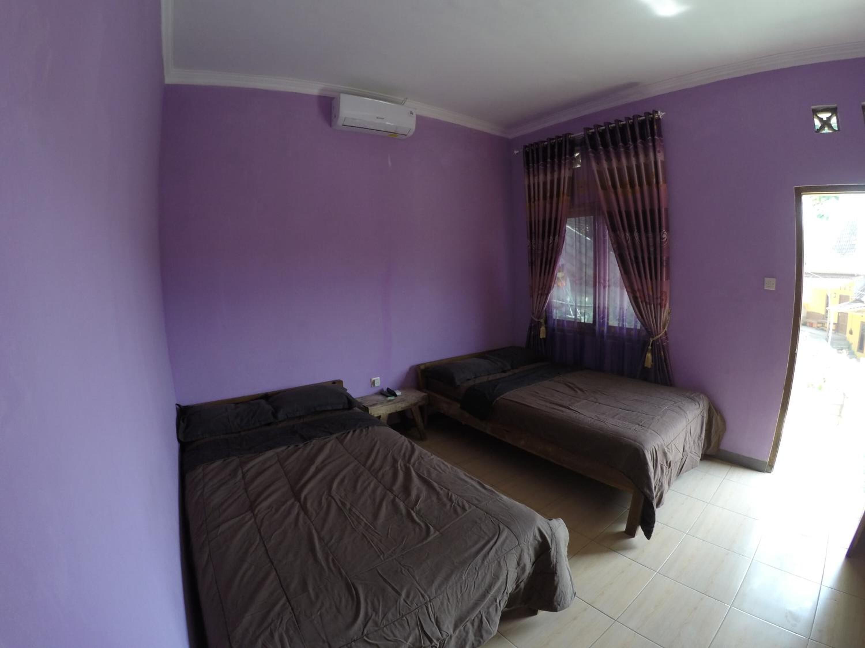 A room with purple walls, two beds, a small table, and a window with curtains.