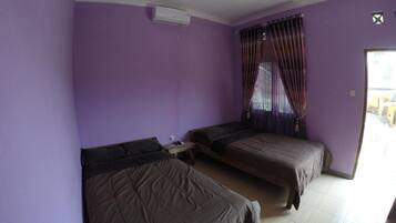 A room with purple walls, two beds, a small table, and a window with curtains.
