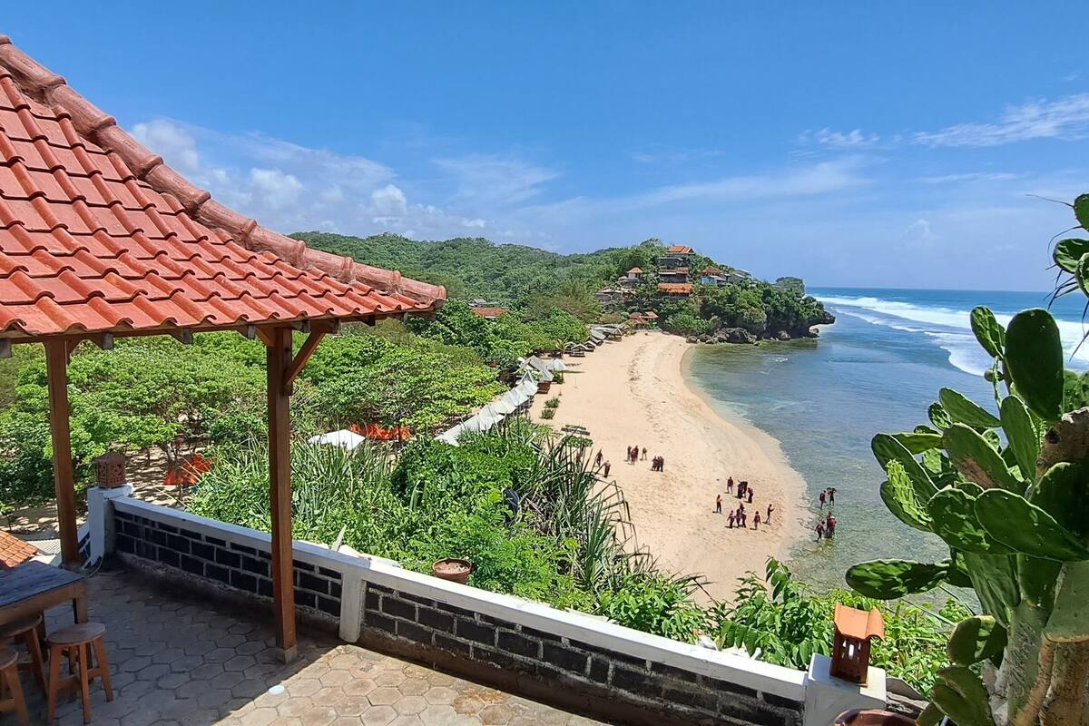 A beach with a red-tiled roof structure, a sandy shore, and lush greenery.