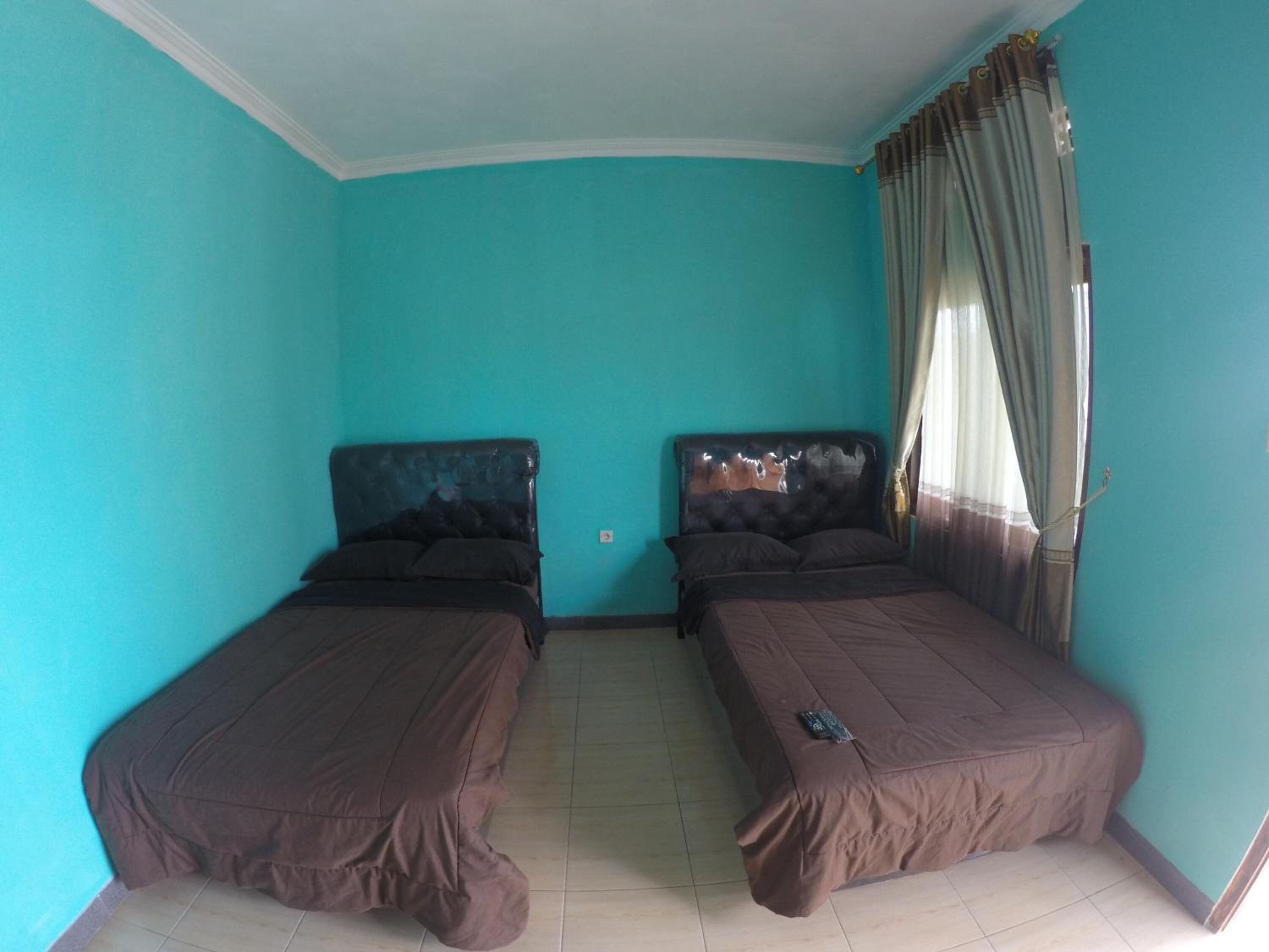 A room with two beds, teal walls, and a window with curtains.