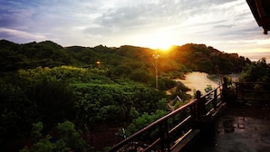 A scenic view from a balcony overlooking a coastal road with lush greenery and a sunset. - Omah Sundak Homestay (Wonosari)