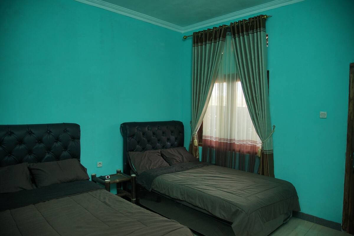 A room with two beds, a small table, and a window with curtains.