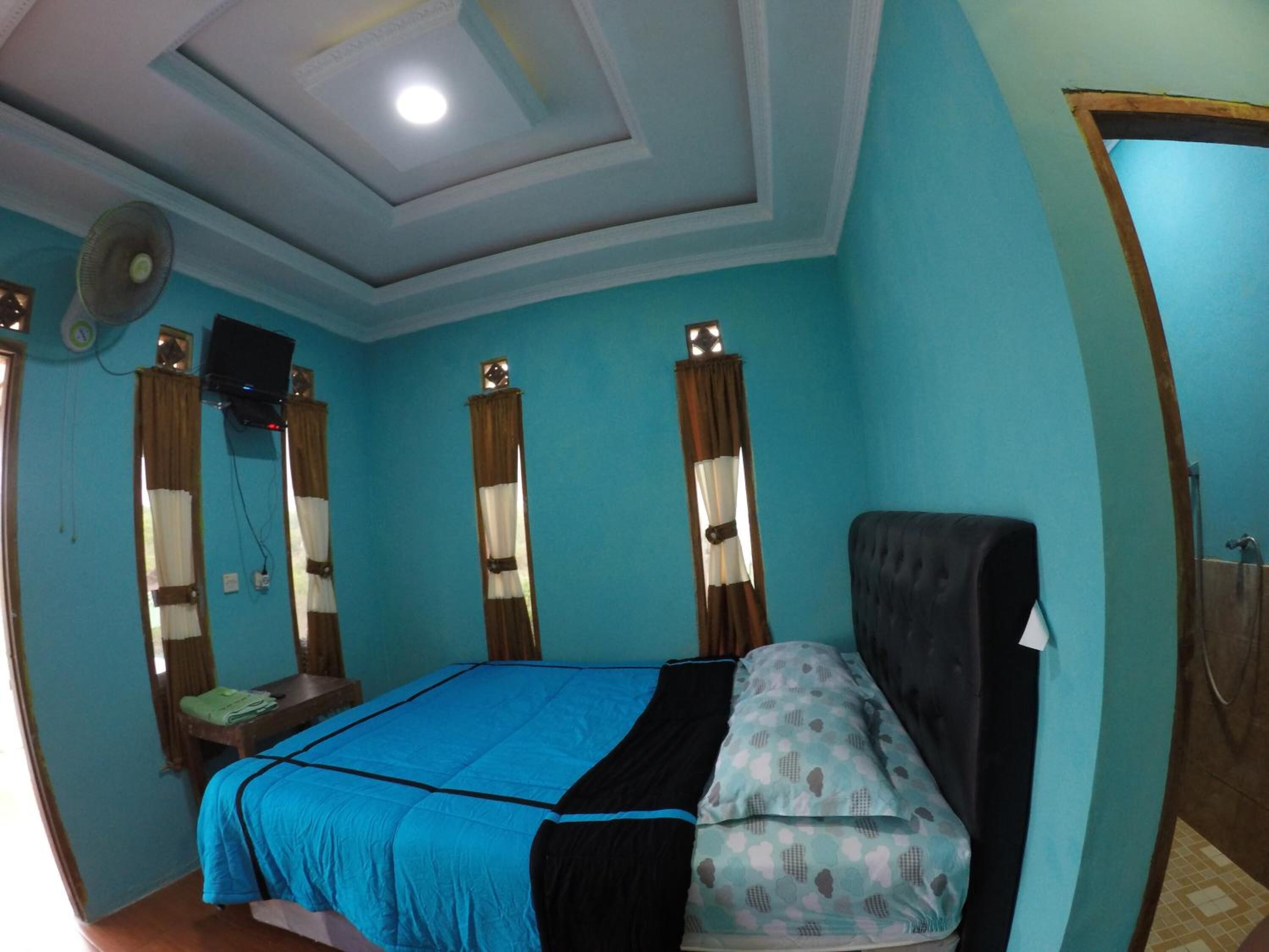 A room with a bed, a desk, a chair, a fan, and a shower area.