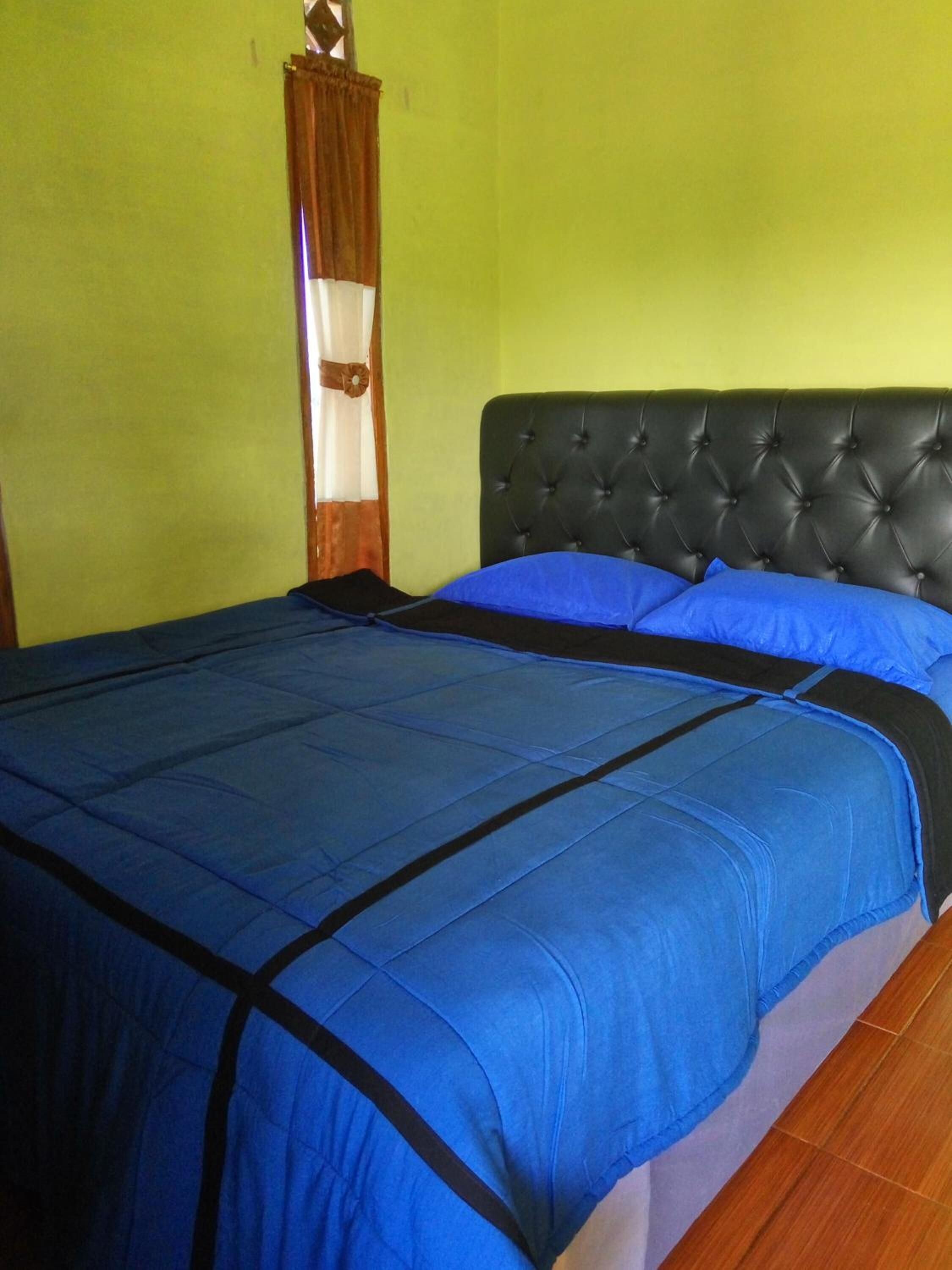 A bed with a black headboard and blue bedding in a room with green walls.