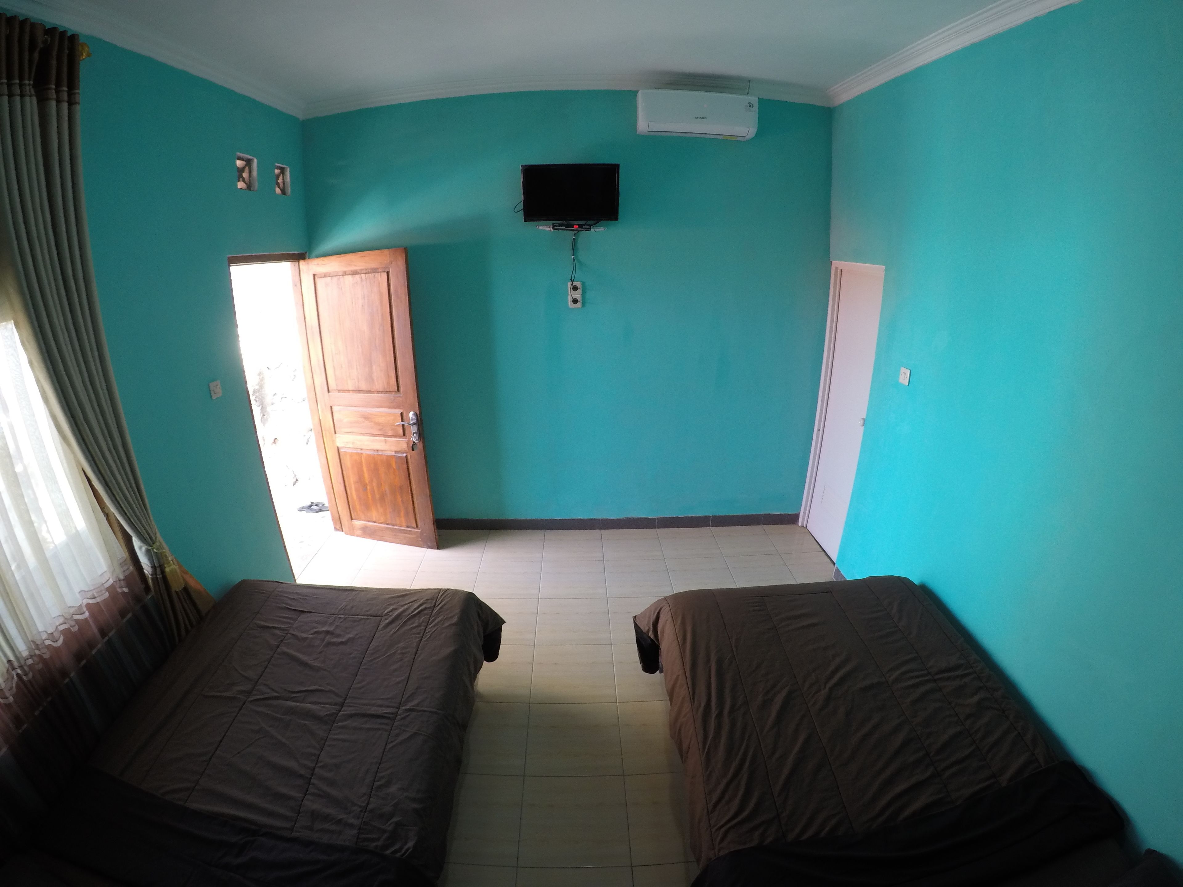 A room with teal walls, two beds, a wooden wardrobe, a television, and an air conditioning unit.