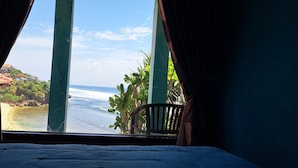A room with a bed and a view of the ocean through curtains. - Omah Sundak Homestay (Wonosari)