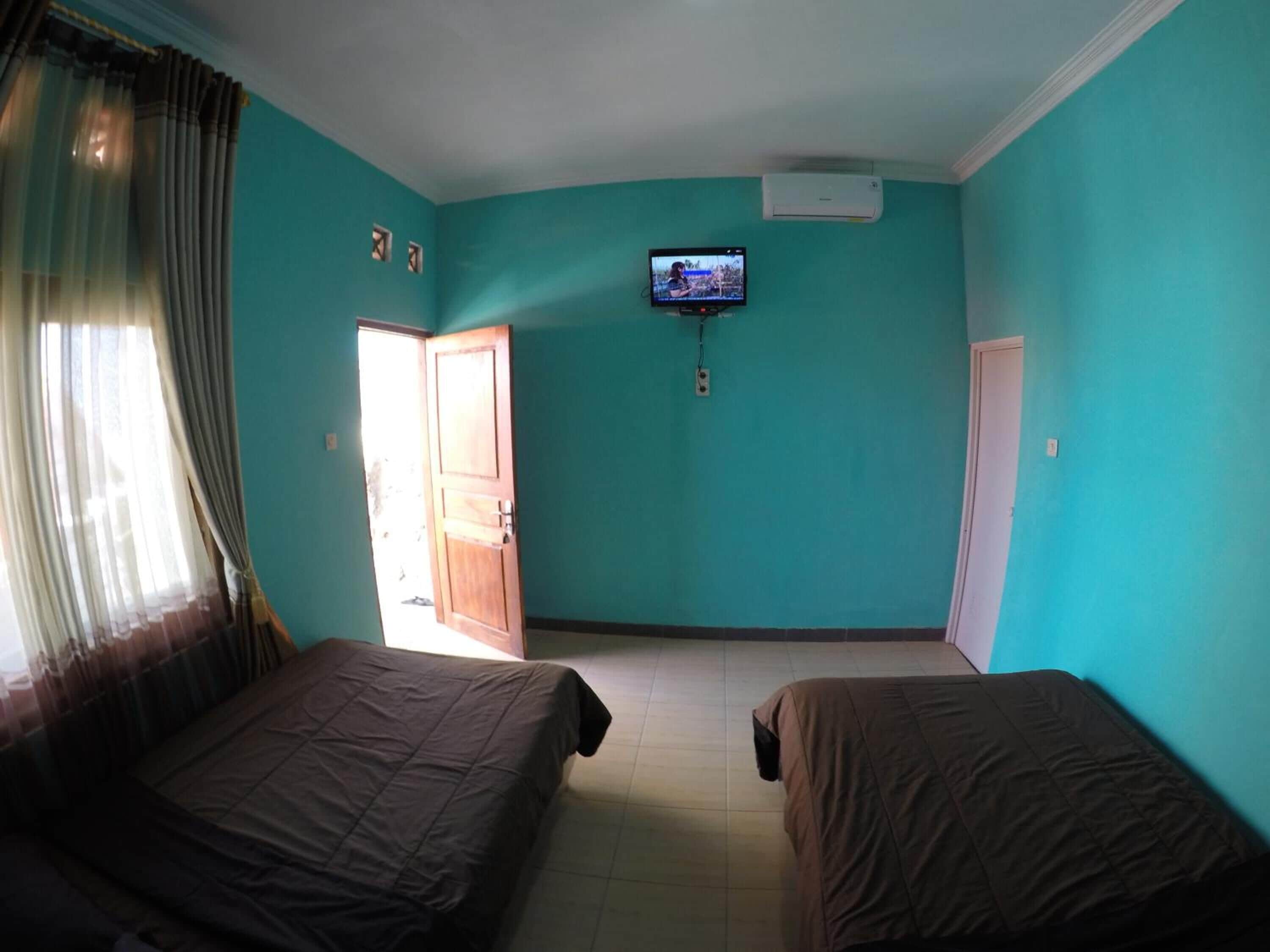 A room with teal walls, two beds, a television on the wall, and a door leading outside.