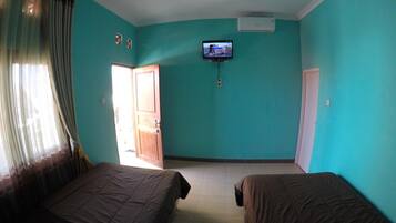 A room with teal walls, two beds, a television on the wall, and a door leading outside.