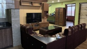 A modern living room with a flat-screen TV, a sofa, a coffee table, and built-in wooden cabinets. - 2BHK Apartment (Siddharthanagar)