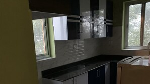 A kitchen with dark cabinets, a stainless steel countertop, and a window providing natural light. - 2BHK Apartment (Siddharthanagar)