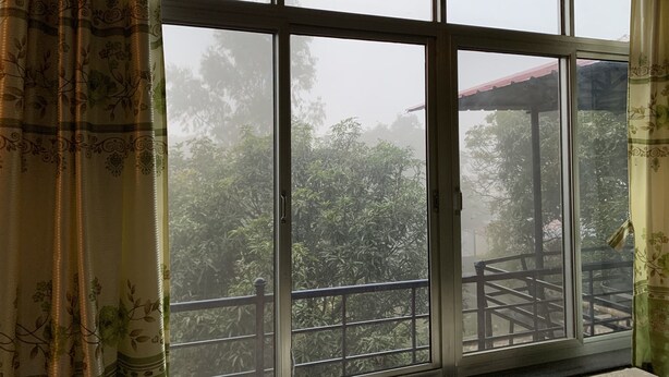 A large window with a view of a balcony and surrounding greenery. - 2BHK Apartment (Siddharthanagar)