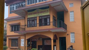 A multi-story building with a sign reading "HEAVENLY GARDEN KIDS CAMPUS PVT. LTD." The building has a red roof, multiple balconies, and a paved courtyard. - 2BHK Apartment (Siddharthanagar)