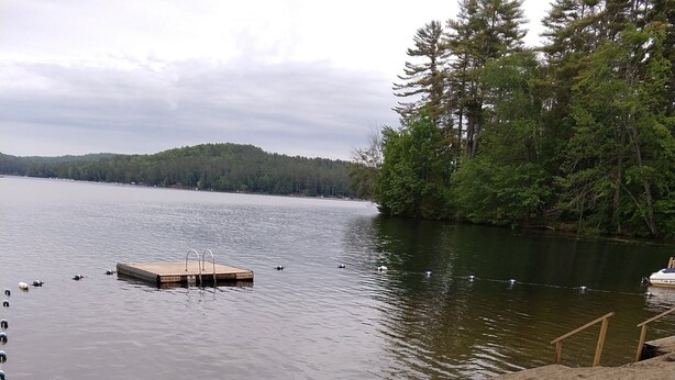Vista con lago, fogata, dos sillas Adirondack y una playa arenosa.