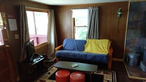 Una sala de estar acogedora con un sofá azul, una mesita y un reposapiés rojo.