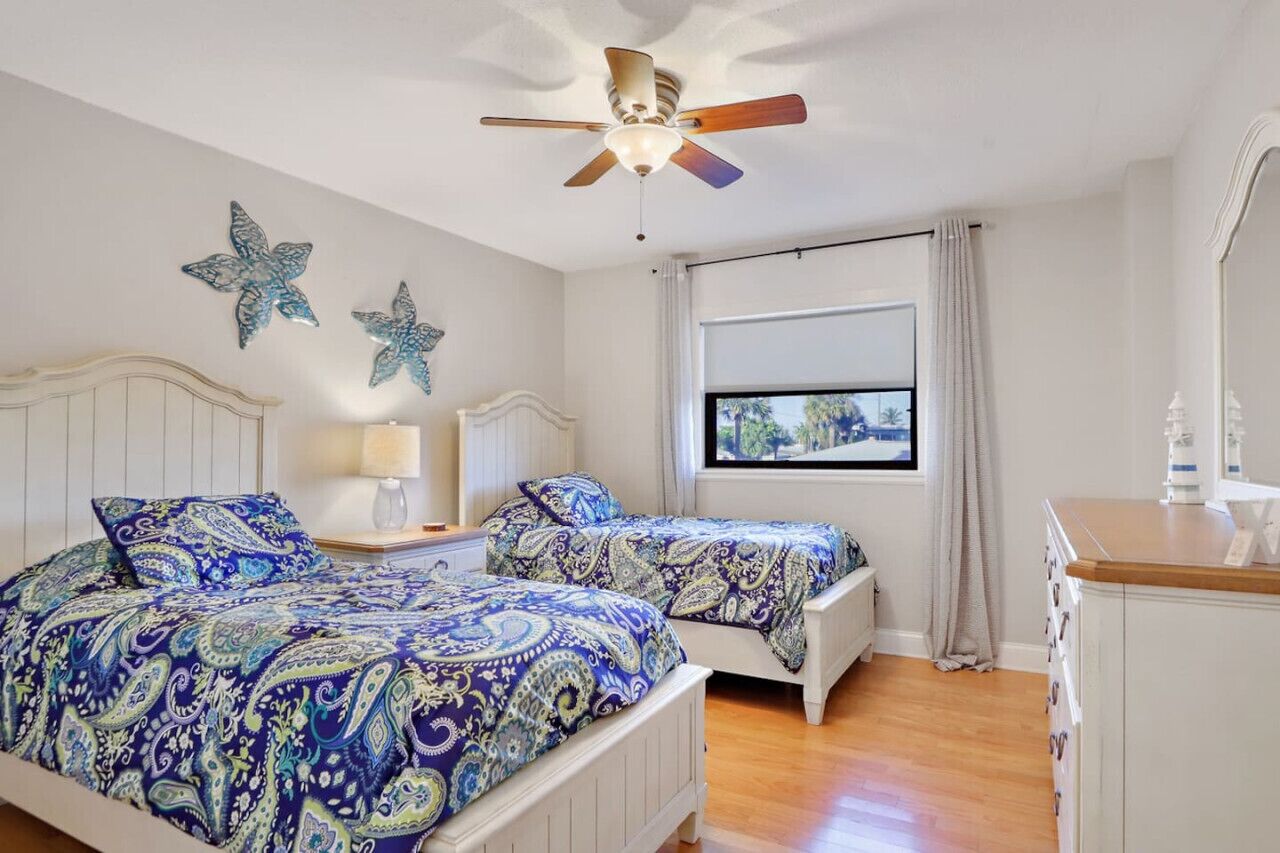 Ein Schlafzimmer mit zwei Betten, einem Deckenventilator, einem Fenster mit Aussicht und dekorativen Seesternen an der Wand.