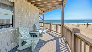 Une terrasse en bois avec des fauteuils Adirondack et une table, donnant sur une plage.